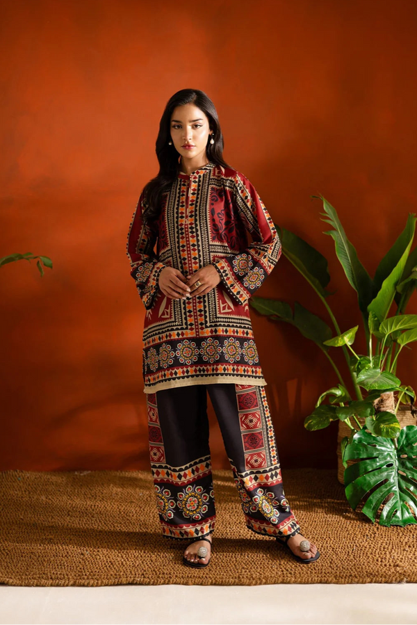 Woman in traditional embroidered outfit standing against an orange wall with a plant.